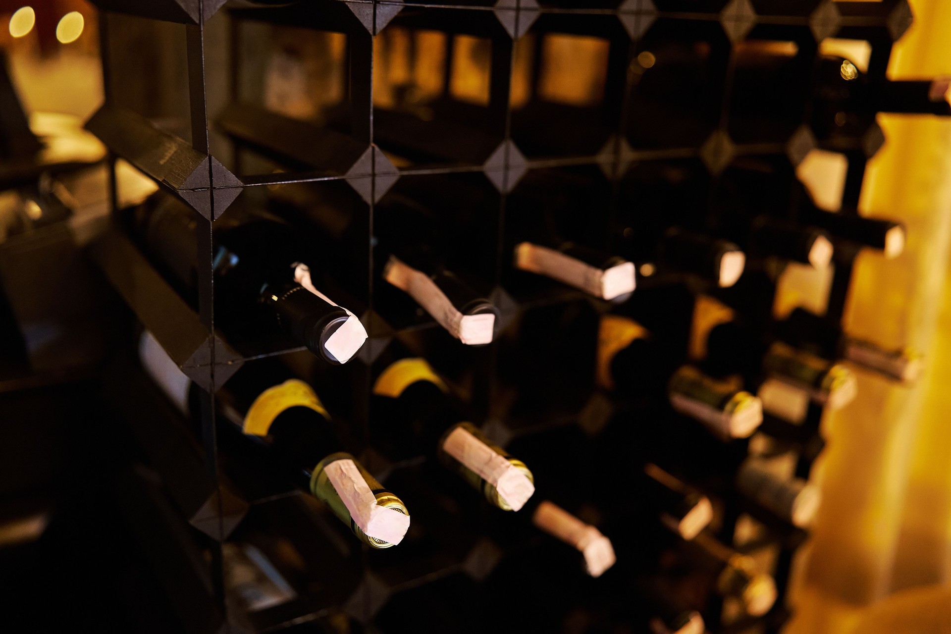 Botellas de vino cuidadosamente almacenadas en un estante de madera en una bodega con poca luz, con varias etiquetas y colores